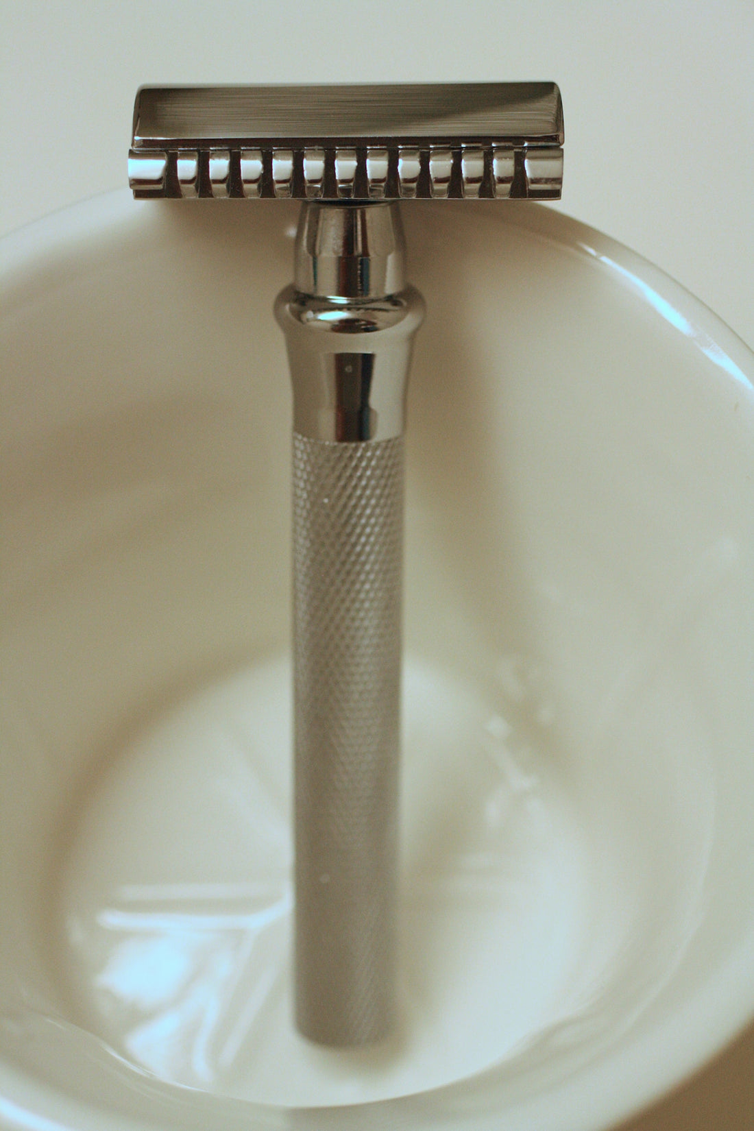A silver double edge safety razor in a bowl