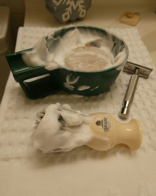 A shaving bowl, brush, and razor with white lather.