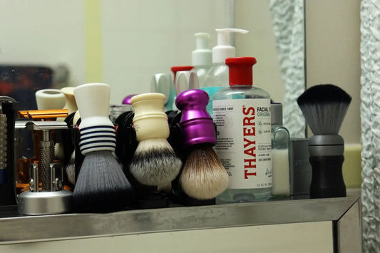 Multiple shaving brushes and skincare products on a bathroom shelf.