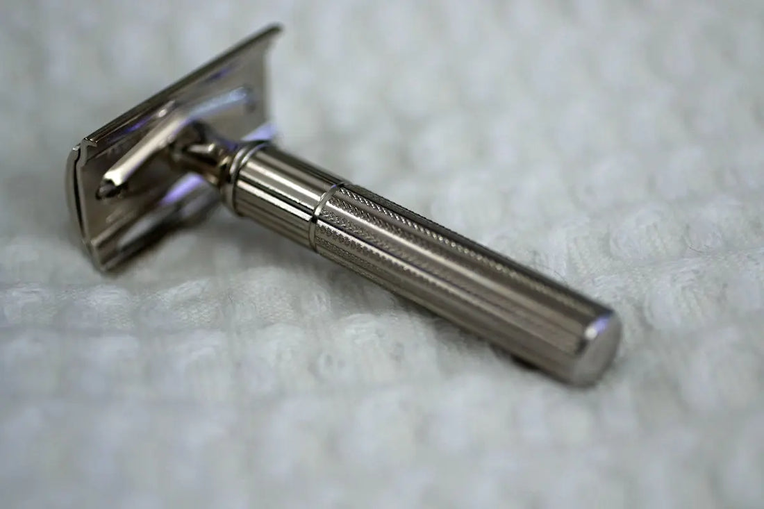 A classic silver safety razor on a textured white surface.