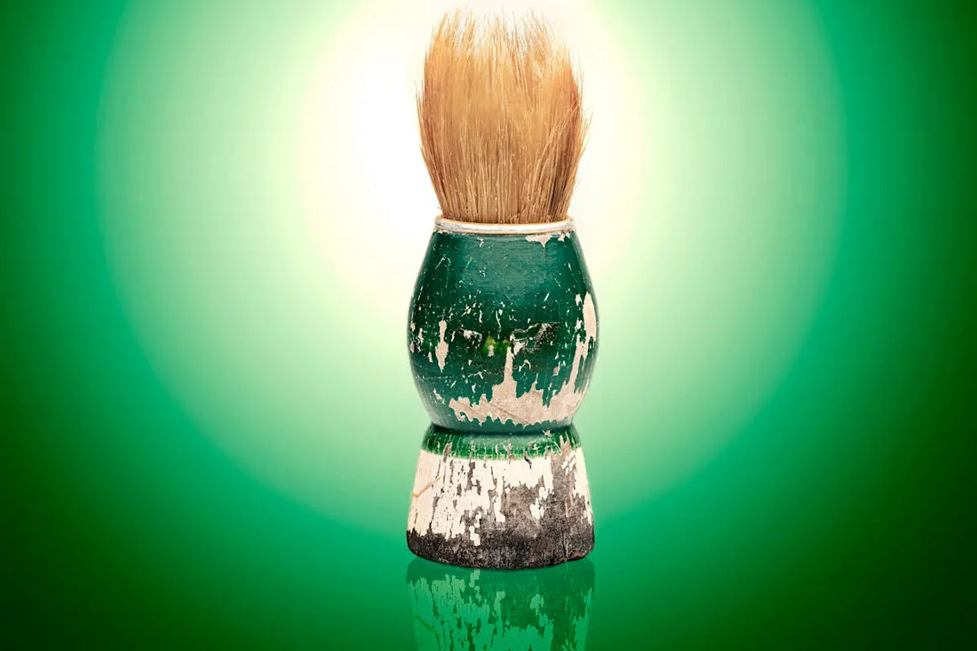Distressed vintage shaving brush on a reflective green background.