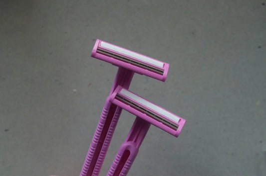 Two pink disposable razors held against a plain grey background