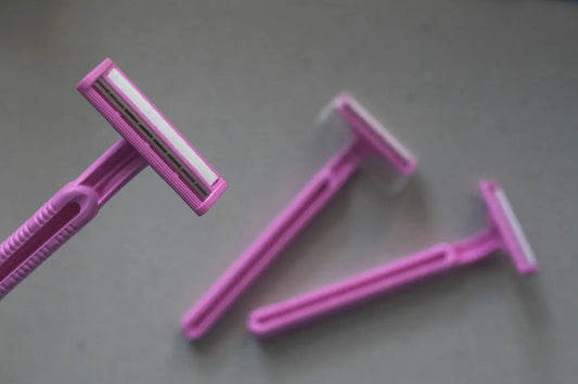 Three pink disposable razors arranged on a plain grey surface